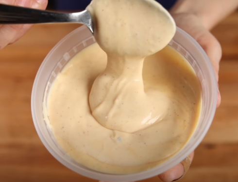 Image of yum yum sauce in a rounded container, dripping from a spoon