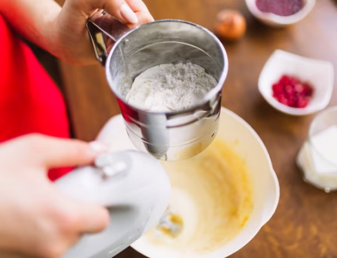 A person pouring flour and vigorously blending batter