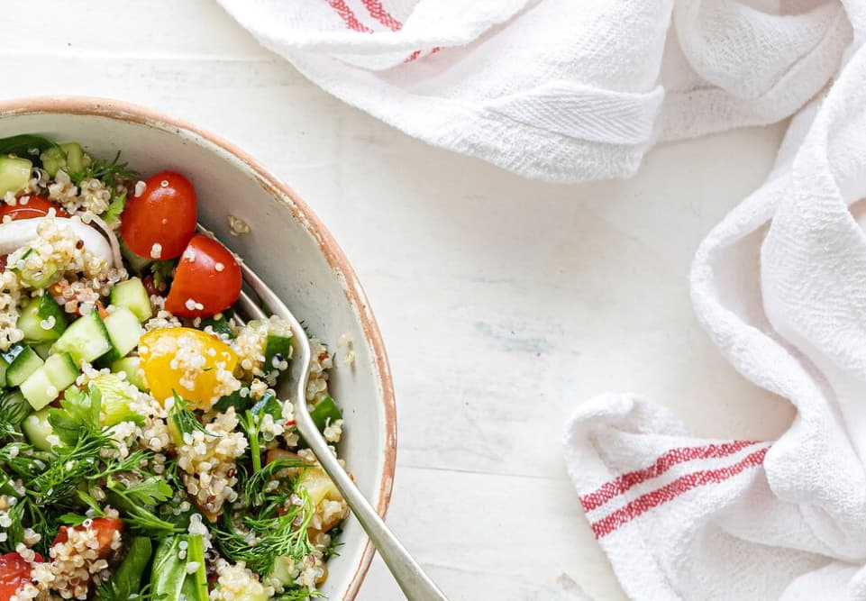 a white towel, bowl of quinoa with cucumbers and tomatoes on the white table