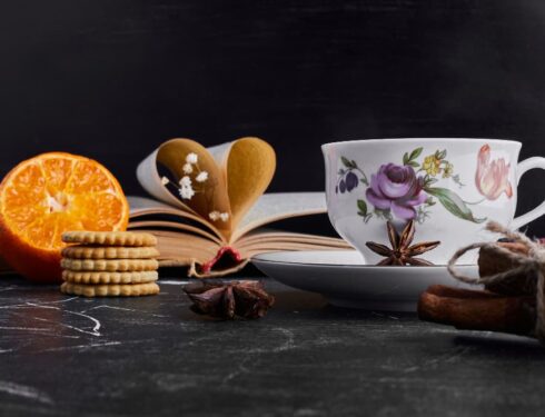 A cozy reading nook with an open book, orange, biscuits, and a floral teacup