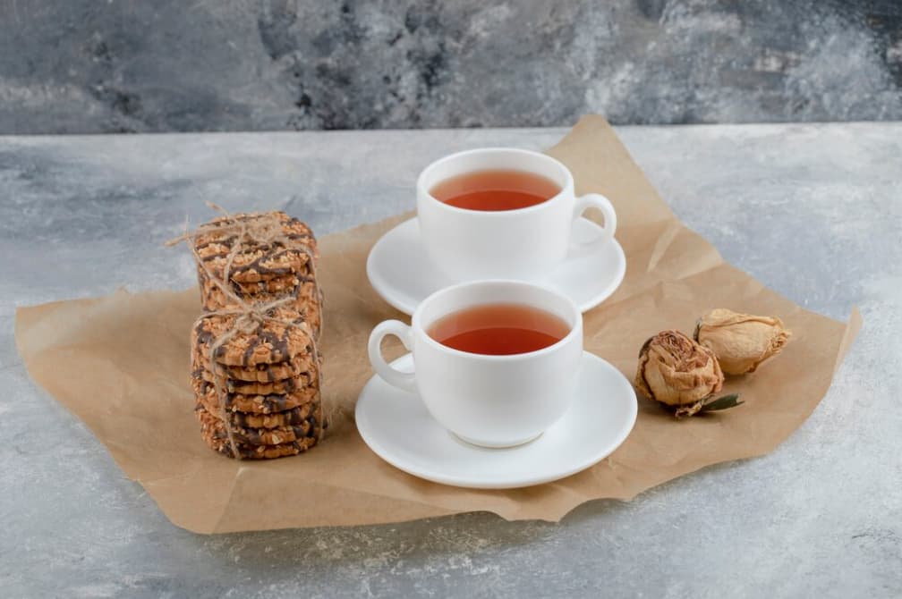 Two cups of tea with cookies on a rustic table, alongside dried roses