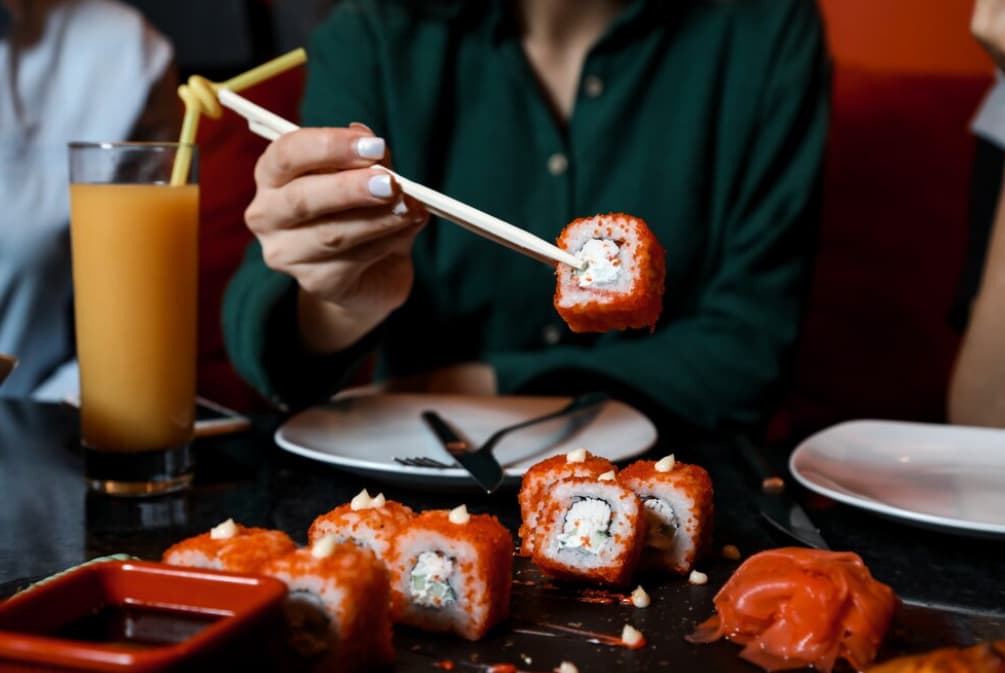 A person is using chopsticks to eat a sushi roll with orange tobiko