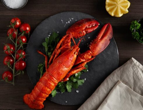 a lobster with herbs on the black plate, cherry, towel, and lemon on the table